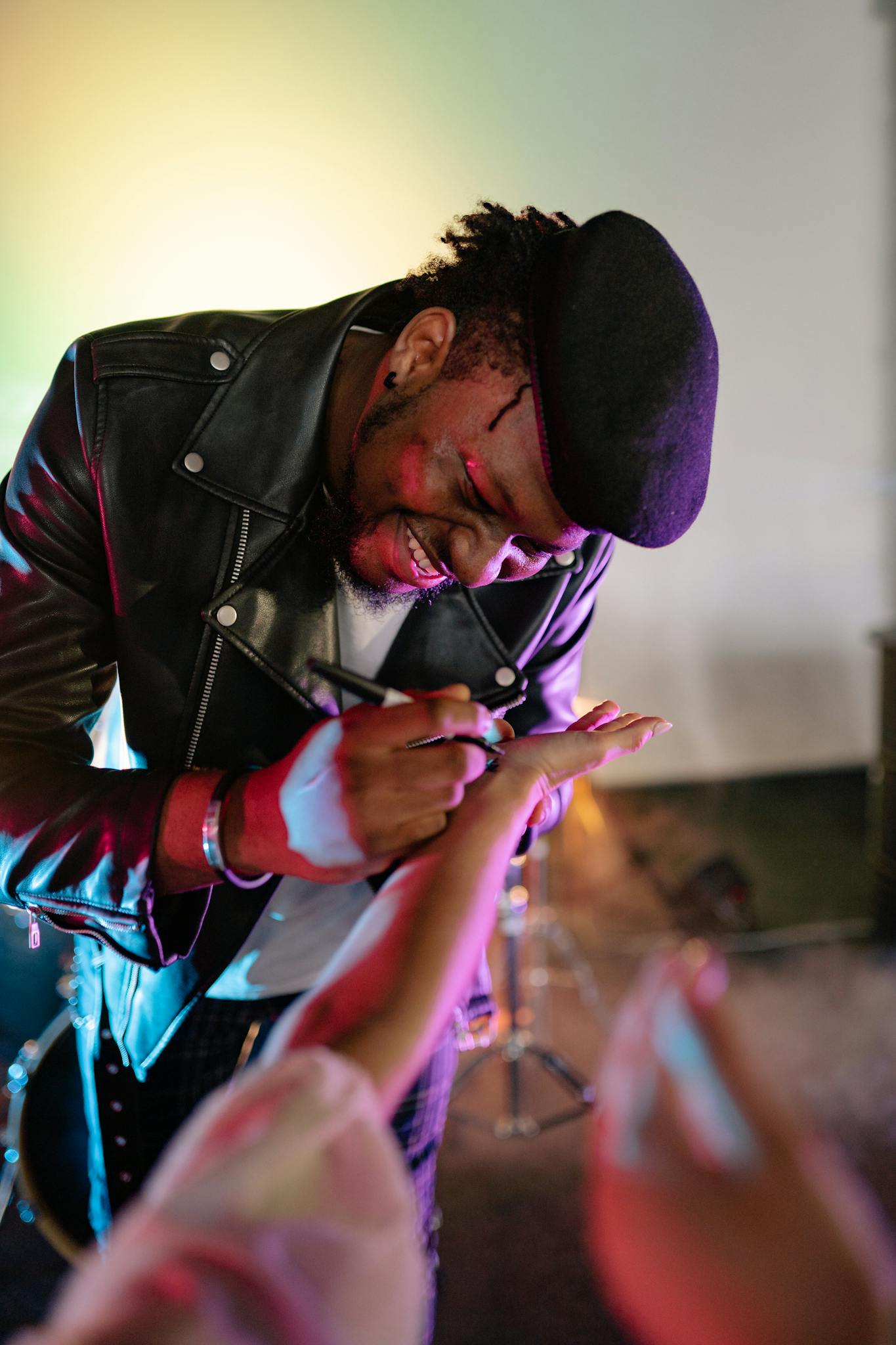 A smiling musician in a black leather jacket signing autographs at a concert.
