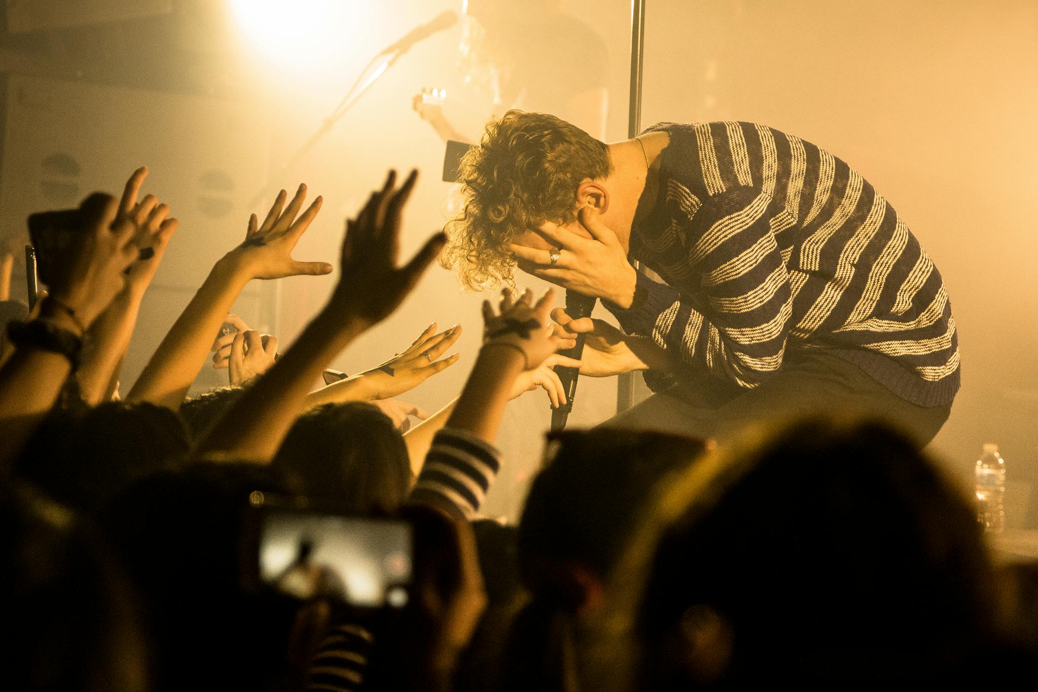 Energetic male musician in striped sweater engages with enthusiastic concert crowd.